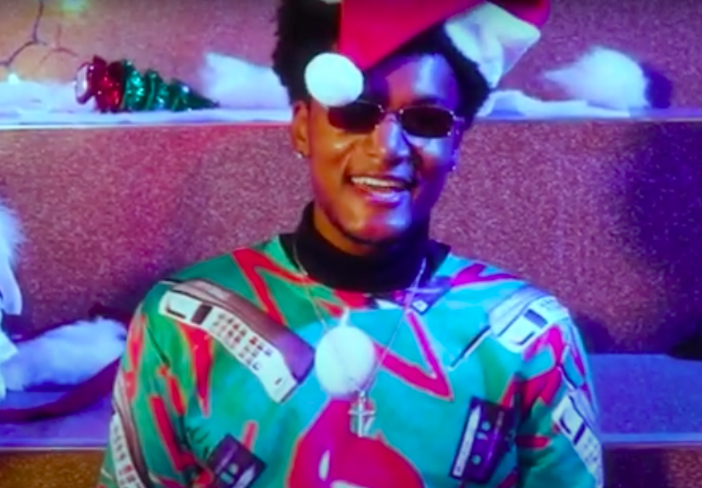 screenshot of a man wearing a Santa hat and a holiday shirt with sunglasses 