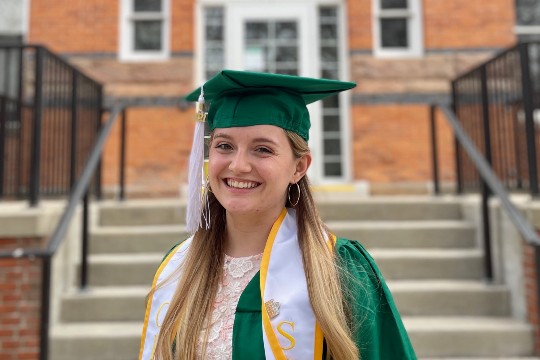 a girl with blonde long hair wearing a green cap and gown
